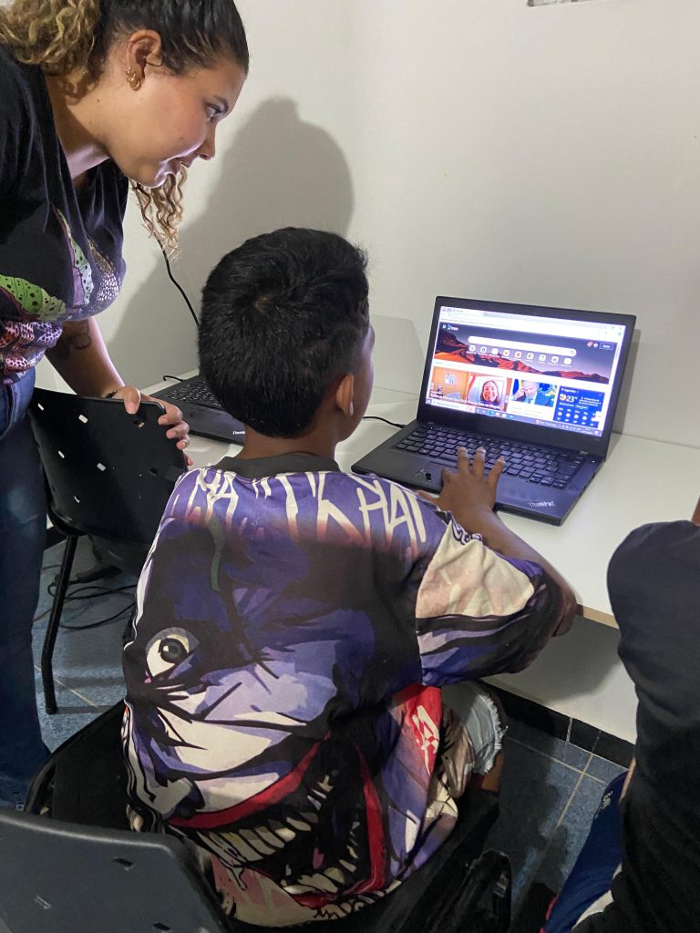crianca mexendo no computador com ajuda de educadora