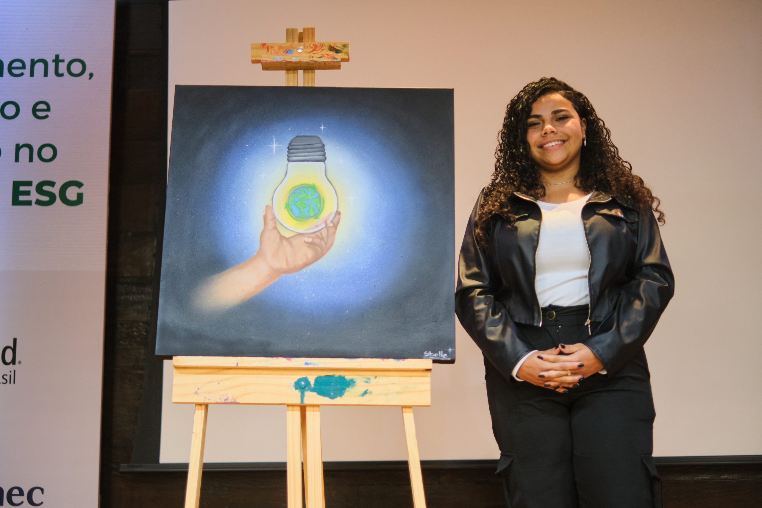 Jovem posa ao lado do quadro que pintou, que ilustra um globo terrestre