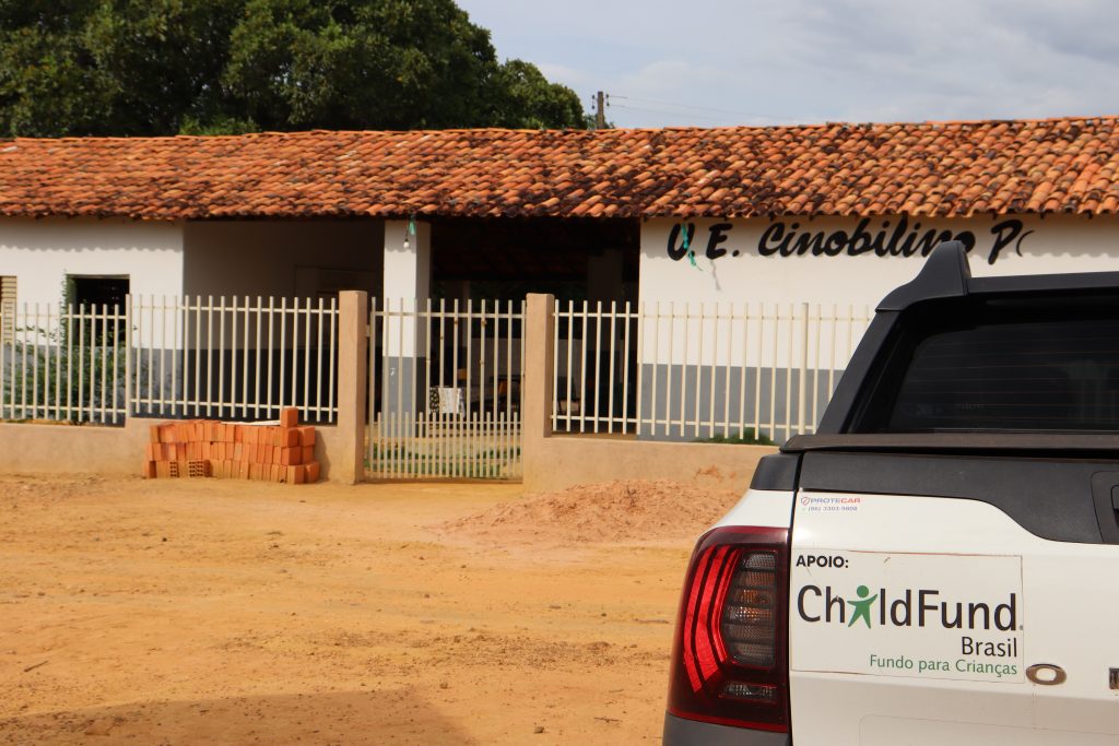 Fachada de escola com carro à frente, com adesivo do ChildFund